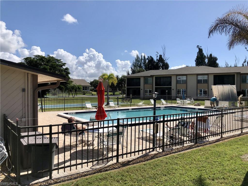 Communal swimming pool with a surrounding paved deck, black metal fencing, and chaise lounges