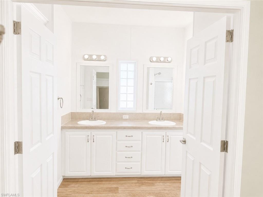 Bathroom with a dual vanity featuring white cabinetry, integrated sinks, light-toned countertop, and individual mirrors with vanity lighting