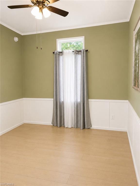 Room featuring wood-finish flooring, wainscoting, and a ceiling fan with integrated lighting