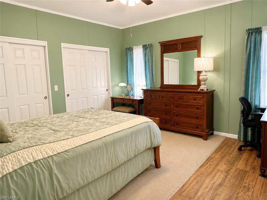 Bedroom featuring a ceiling fan, two white paneled sliding closet doors, and wood-finish flooring extending into the space
