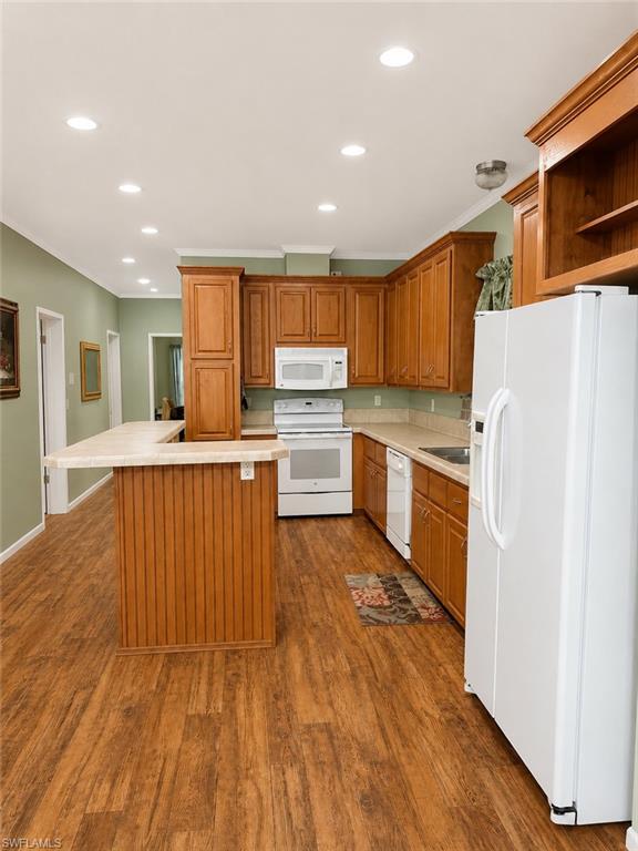 Kitchen featuring wood-finish flooring, wood cabinetry, white appliances, a breakfast bar, and recessed lighting
