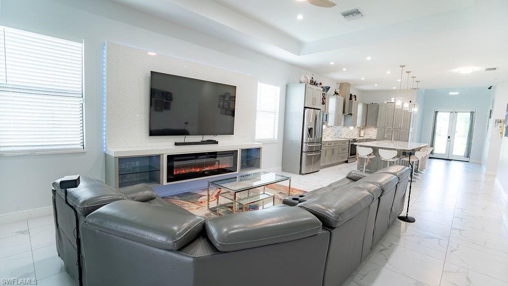 Open-concept living space with large format tile flooring and tray ceiling