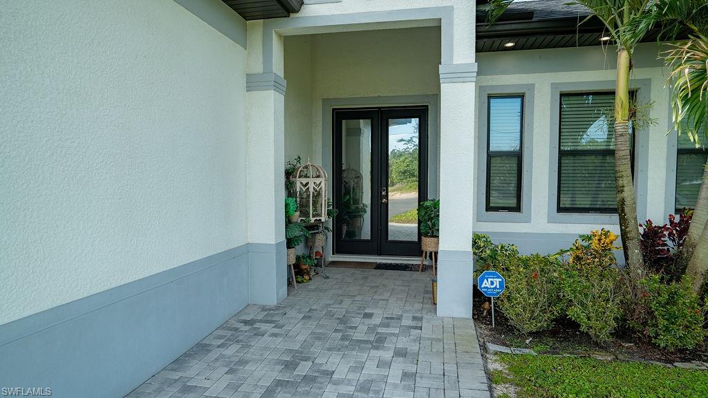 Columned entry with double glass-paneled doors, paver walkway, stucco exterior, and accent landscaping