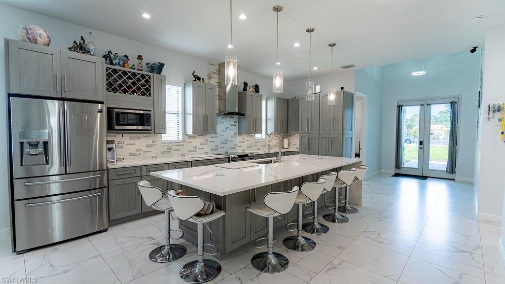 Open-concept kitchen featuring an expansive island with seating, stainless steel appliances, grey cabinetry, a tile backsplash, and contemporary pendant lighting