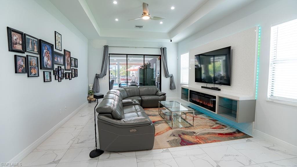 Living space featuring tray ceiling with recessed lighting, porcelain tile flooring, built-in entertainment center with electric fireplace, and sliding glass doors to the exterior