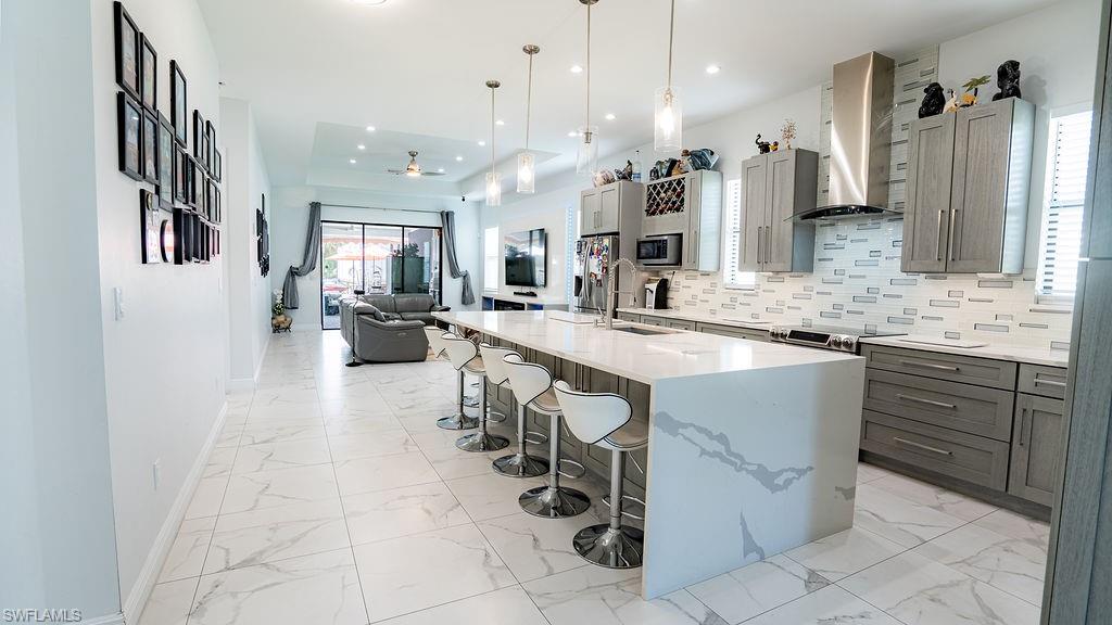 Contemporary kitchen featuring an oversized island with waterfall countertop, pendant lighting, stainless steel appliances, and grey cabinetry