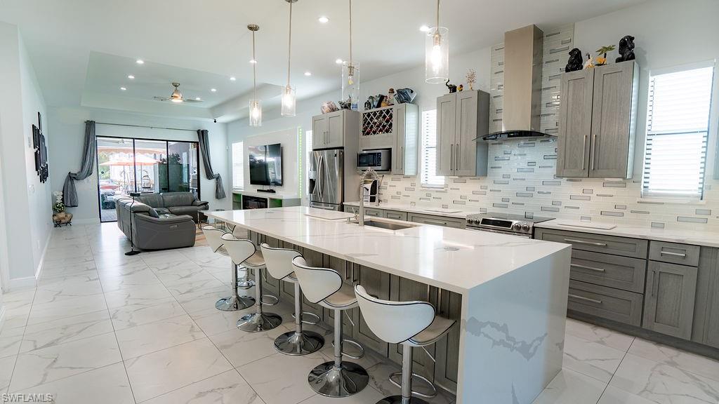 Open concept living space featuring a spacious kitchen island with seating, stainless steel appliances, a modern tile backsplash, and large format tile flooring