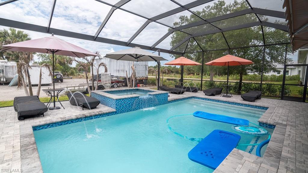 Screened pool area featuring a blue tiled spa with waterfall, paver decking, and clear water