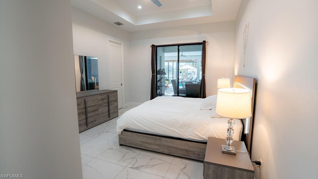 Bedroom featuring marble-look tile flooring, a tray ceiling with recessed lighting, and a ceiling fan