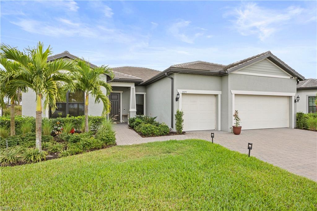 Ranch-style home with a front lawn, decorative driveway, stucco siding, an attached garage, and a tiled roof