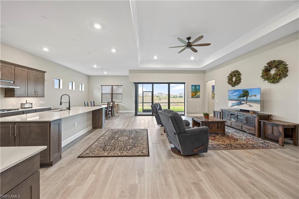 Kitchen with open floor plan, light stone counters, light wood-style flooring, dark brown cabinetry, and an island with sink