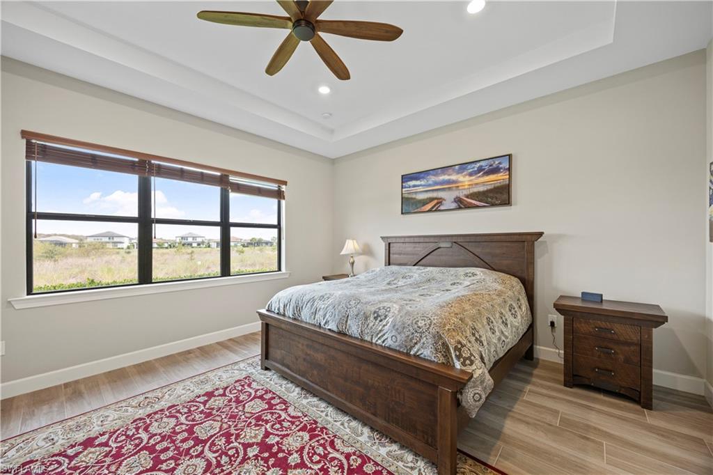 Bedroom featuring a raised ceiling, light wood-type flooring, ceiling fan, and recessed lighting
