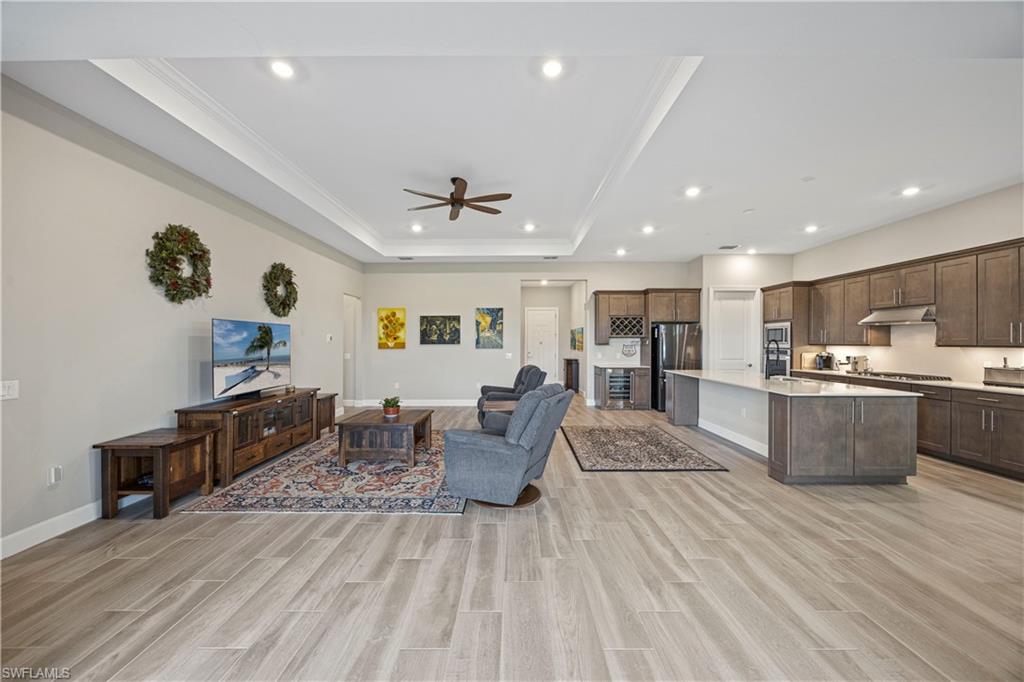 Living room with wood finish floors, a ceiling fan, a raised ceiling, recessed lighting, and crown molding