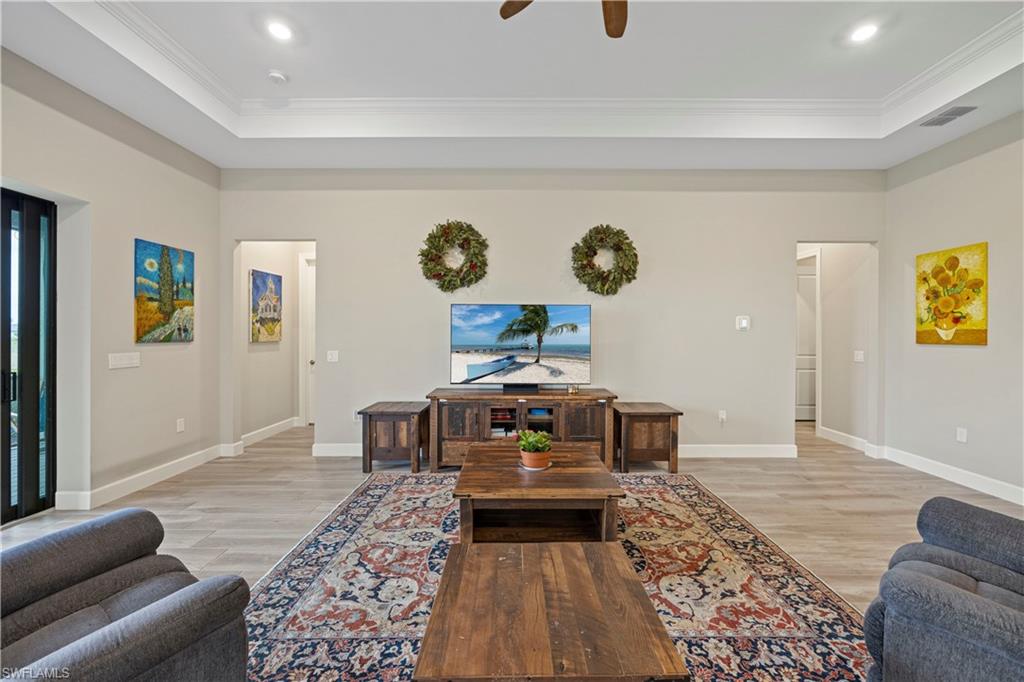 Living room featuring light wood-type flooring, a ceiling fan, ornamental molding, a raised ceiling, and recessed lighting