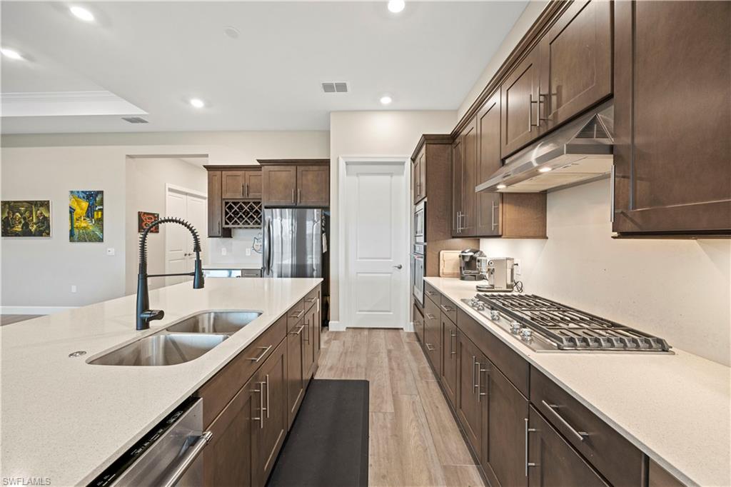 Kitchen with light wood-type flooring, light stone countertops, recessed lighting, under cabinet range hood, and dark brown cabinets