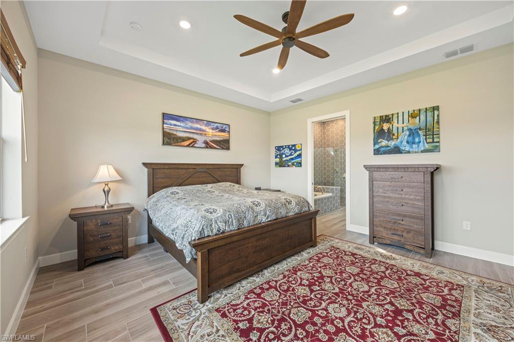 Bedroom with wood tiled floors, ceiling fan, a raised ceiling, recessed lighting, and connected bathroom