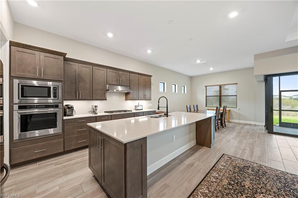 Kitchen with stainless steel appliances, finishes, dark brown cabinets, wood finish floors, a kitchen island with sink, and recessed lighting