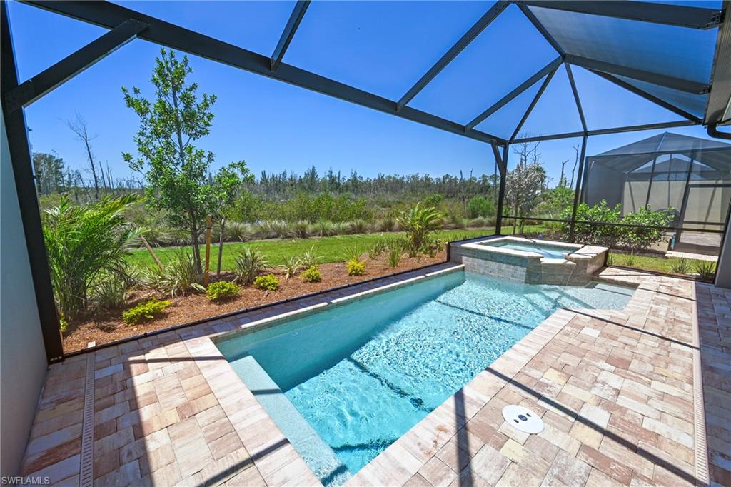 Screened outdoor living area featuring a rectangular pool with integrated spa and paver decking
