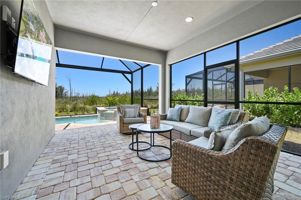 Screened lanai featuring a paver patio, integrated swimming pool with a waterfall feature, and a stucco exterior wall with a mounted television