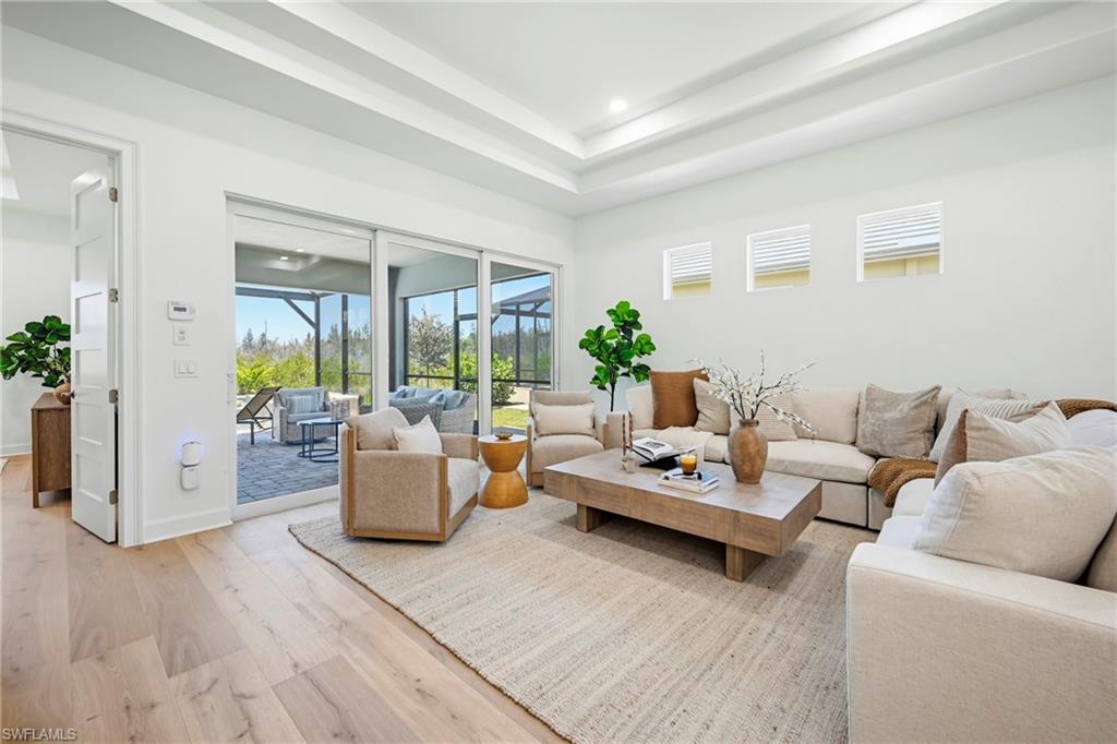 Open concept living area featuring light wood-finish flooring, a tray ceiling, and sliding glass doors opening to a screened outdoor patio