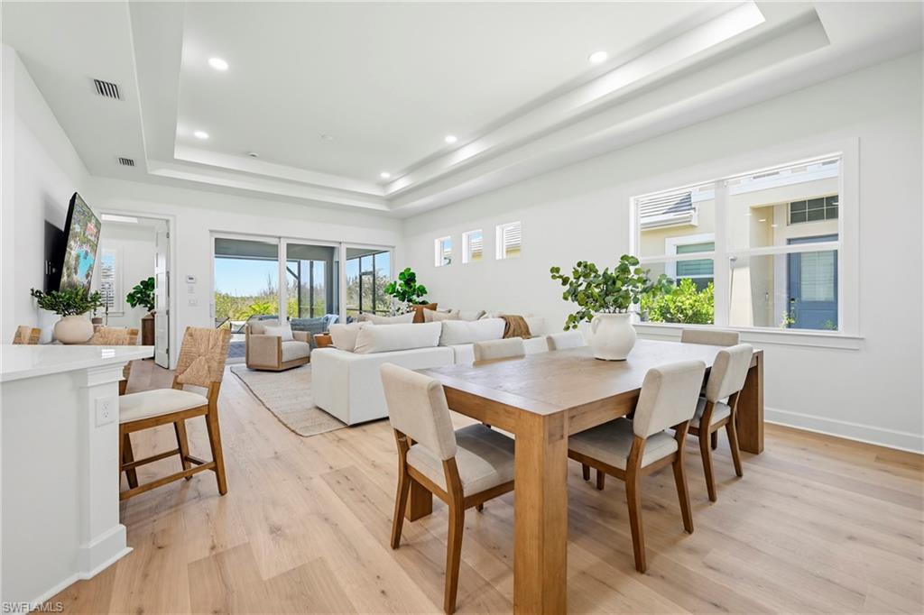 Spacious open-concept living area featuring light wood-finish flooring, a coffered ceiling with recessed lighting, and large sliding glass doors leading to an outdoor space