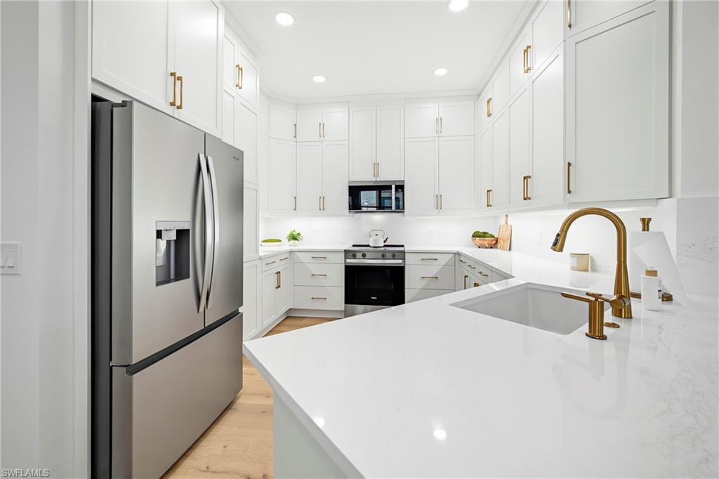 Modern kitchen featuring white cabinetry, light-toned countertops, stainless steel appliances, a brass-finish faucet, and recessed lighting