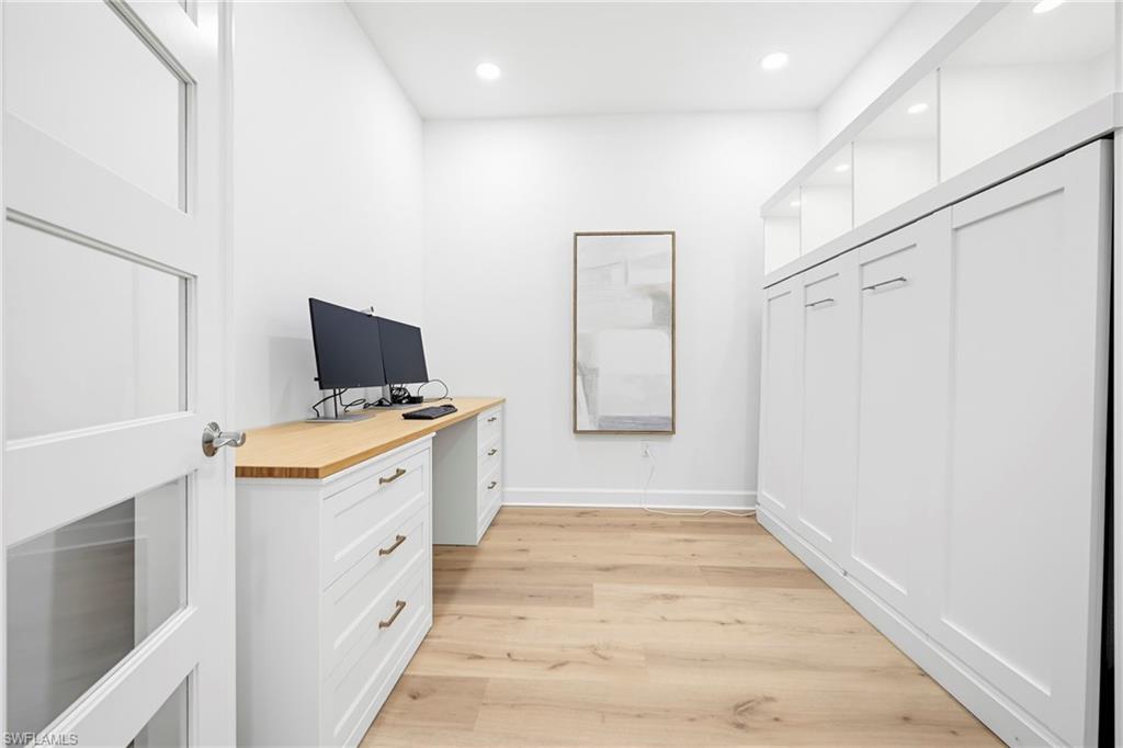Dedicated office space featuring light wood-finish flooring, recessed lighting, and a built-in desk with a natural wood countertop