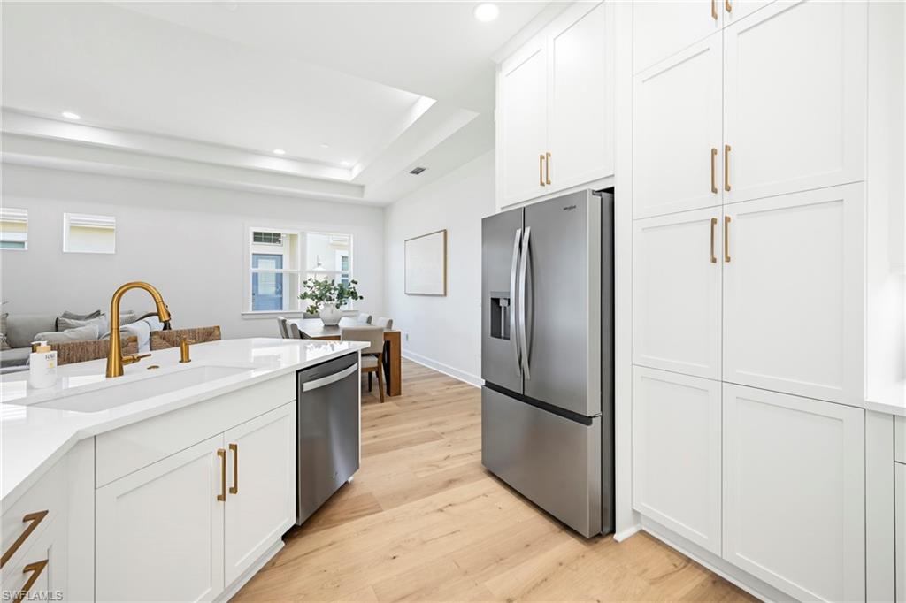 Contemporary kitchen featuring white shaker cabinetry, stainless steel appliances, a large island with an undermount sink, a gold-finish gooseneck faucet, and wood-finish flooring