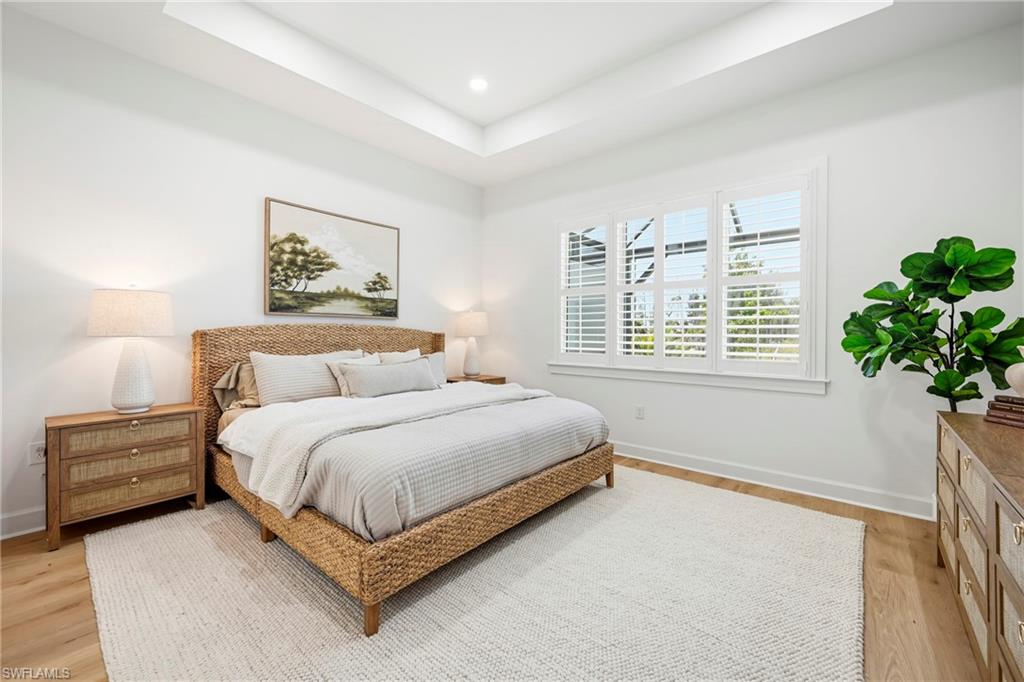 Room featuring wood-finish flooring, a tray ceiling, and multiple windows with plantation shutters