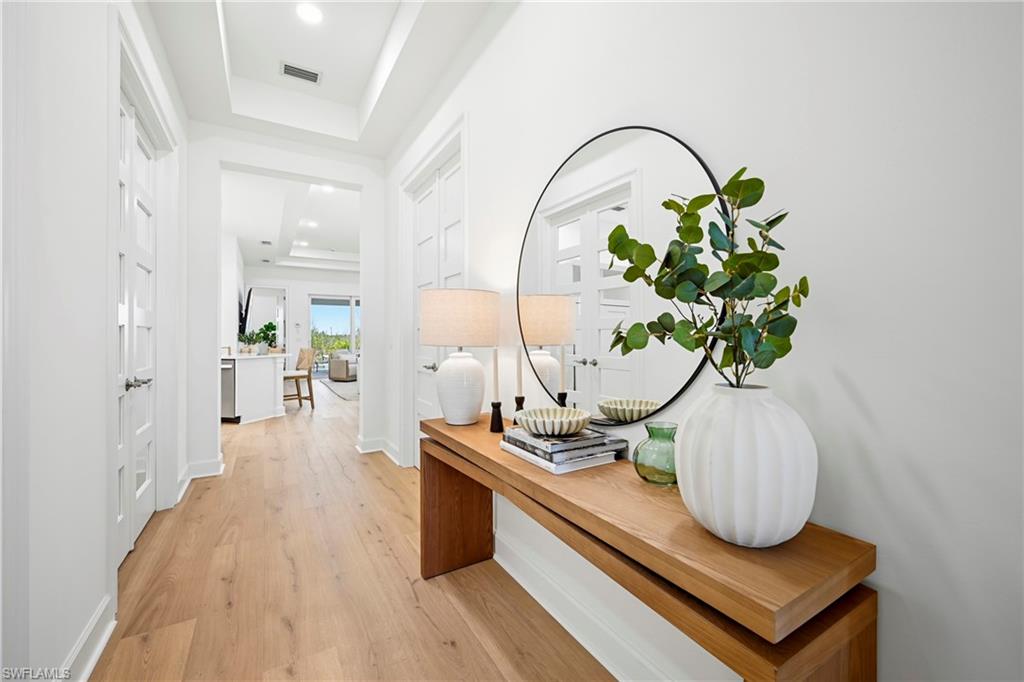 Spacious entryway featuring wood-finish flooring, white paneled doors, and a tray ceiling with recessed lighting