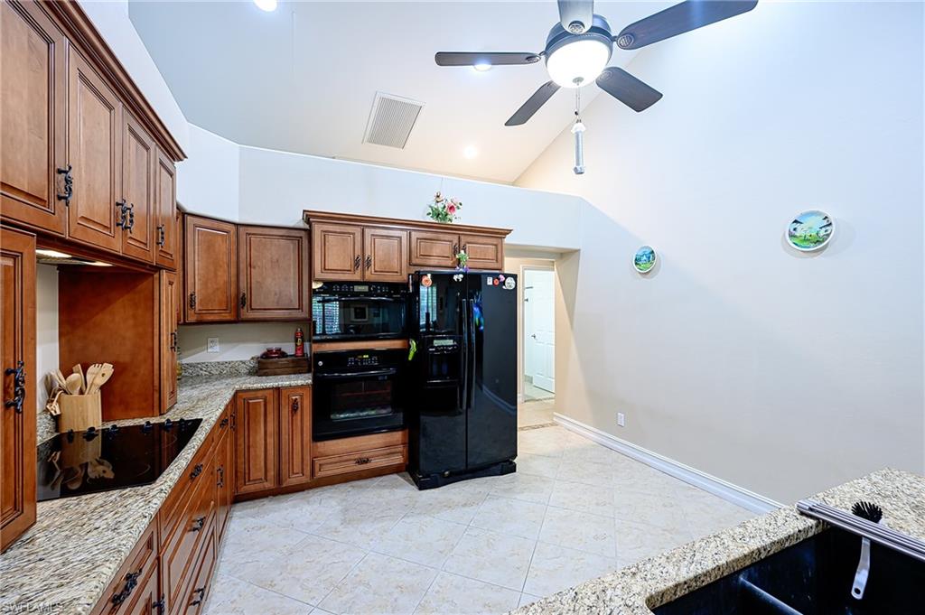 Kitchen featuring high vaulted ceiling, black appliances, ceiling fan, light stone countertops, and light tile patterned flooring