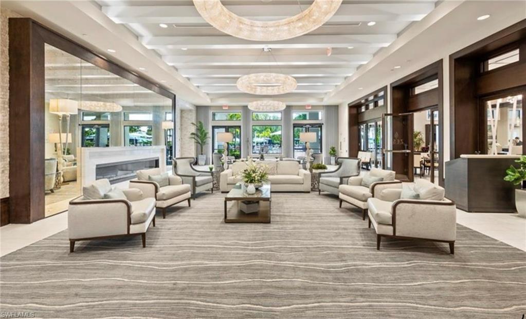 Spacious common area featuring a coffered ceiling with multiple circular chandeliers, a built-in linear fireplace with a stone surround, an expansive area rug, and wood-paneled walls