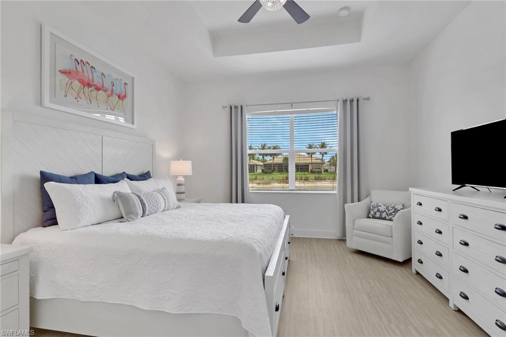 Spacious room featuring wood-finish flooring, a tray ceiling with a ceiling fan, and a large window with horizontal blinds