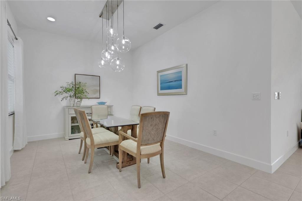Dining area featuring a contemporary chandelier with multiple glass globes, tile flooring, and crisp white walls