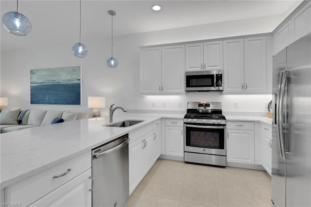 Modern kitchen featuring white cabinetry, stainless steel appliances, light countertops, a stainless steel sink with a gooseneck faucet, and integrated under-cabinet lighting