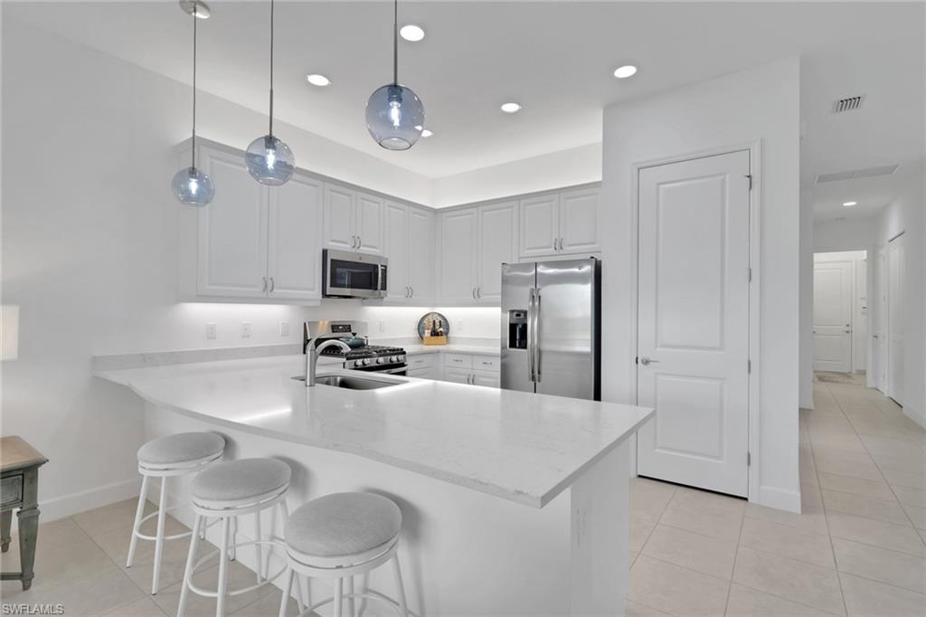 Modern kitchen featuring white shaker cabinetry, stainless steel appliances, a white solid surface countertop, and three spherical pendant lights
