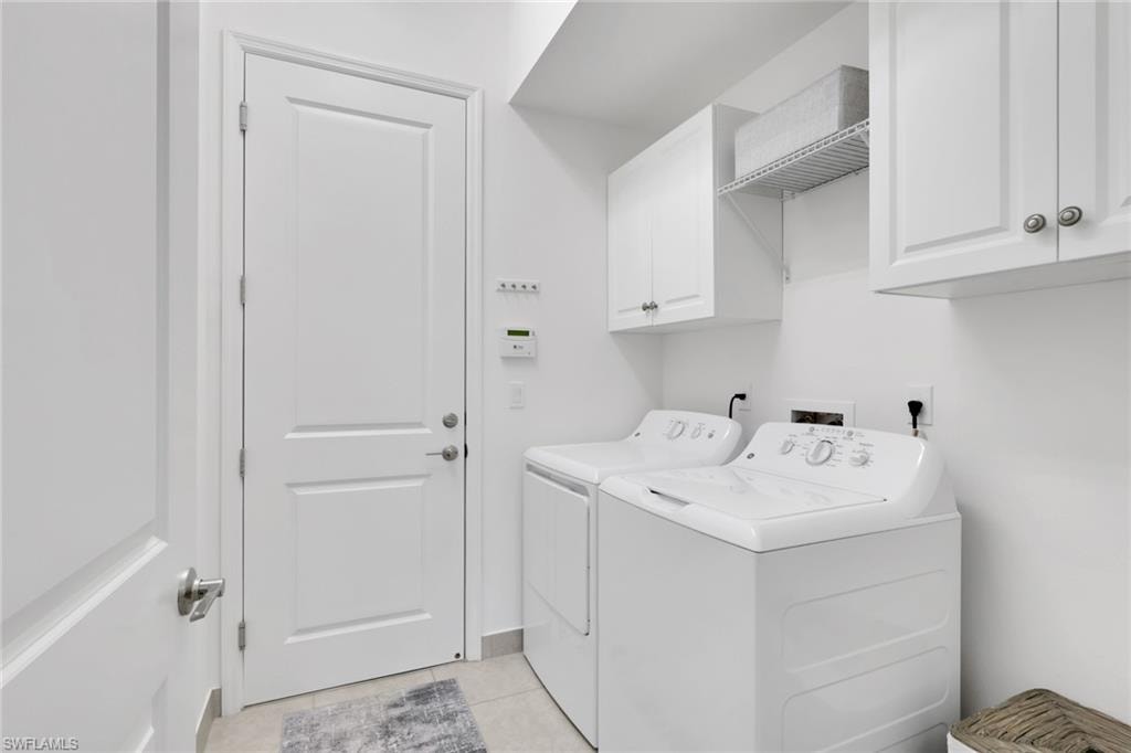 Dedicated laundry area featuring white cabinetry, an open wire shelf, and light-toned tile flooring