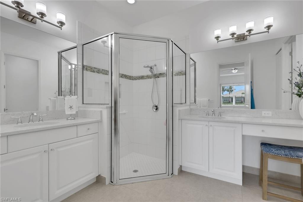 Bathroom featuring a glass-enclosed shower with decorative accent tile, dual vanity sinks, white cabinetry, and a dedicated vanity area