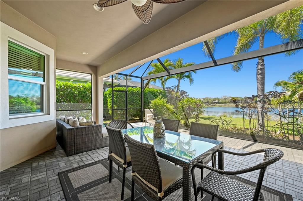 Screened lanai featuring paver flooring, a ceiling fan, and a lake backdrop with mature palm trees