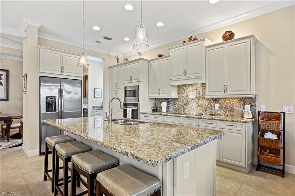 Kitchen featuring a central island with integrated sink, stainless steel appliances, light-toned cabinetry, and tiled flooring