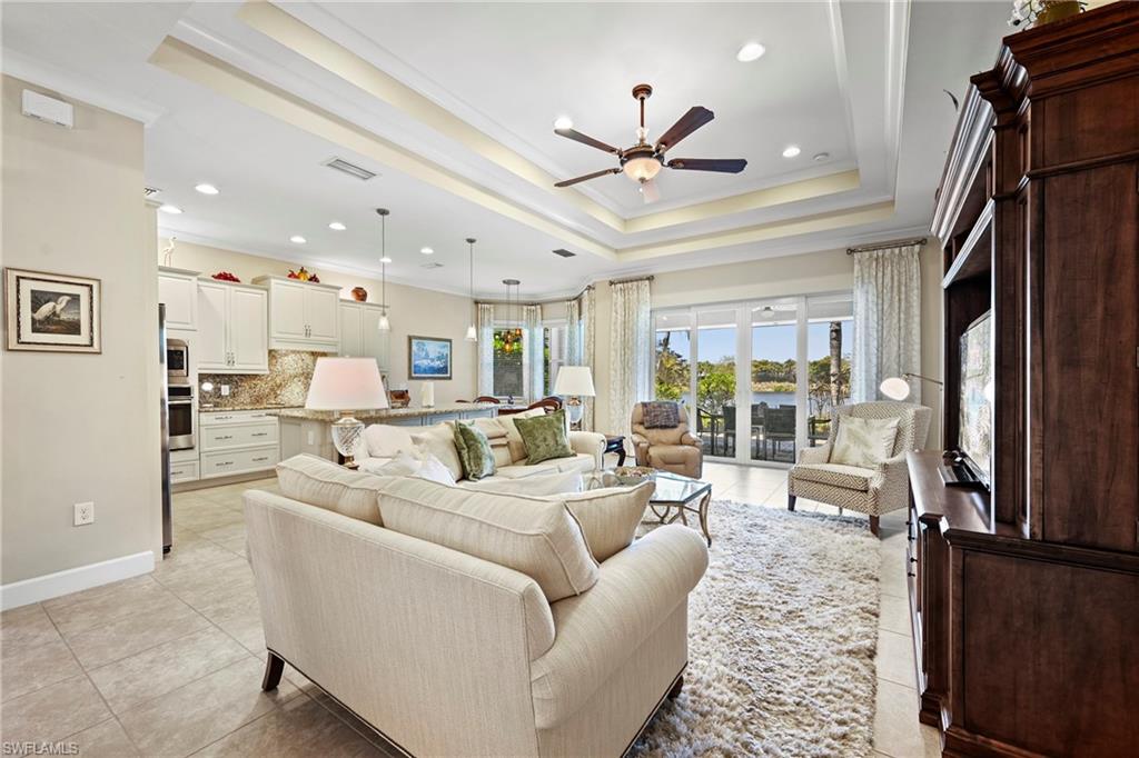 Open-concept living space featuring a tray ceiling with recessed lighting, tile flooring, and a ceiling fan