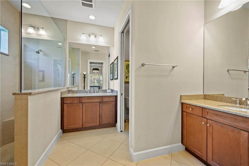 Bathroom featuring a glass-enclosed shower, dual wood-finish vanities with light-toned countertops, and tiled flooring