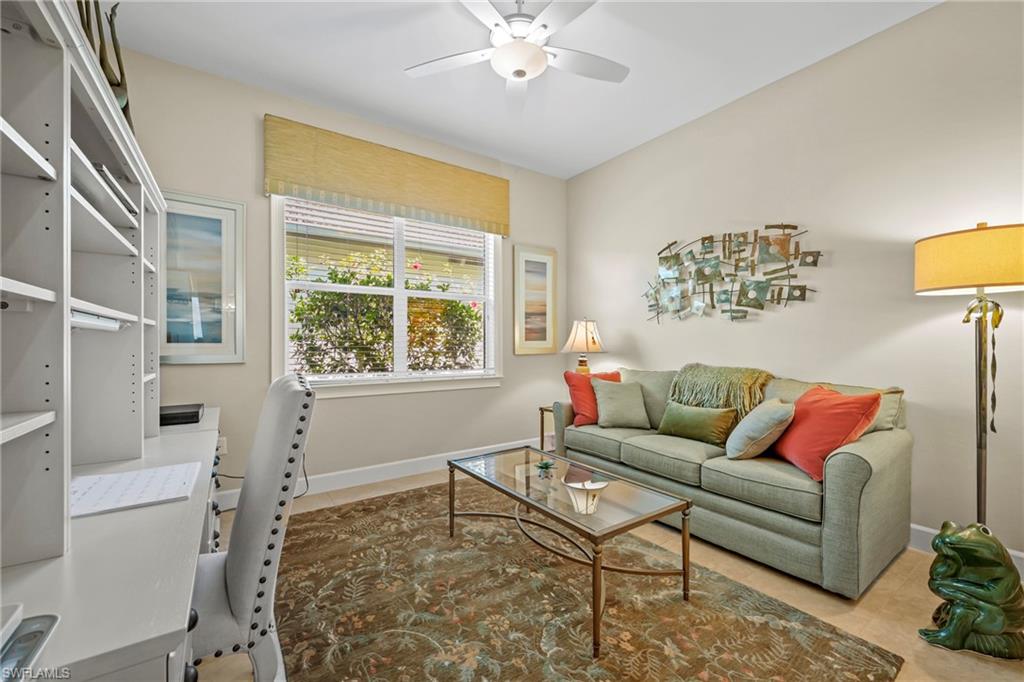 Versatile room featuring a built-in white desk and shelving unit, a large window with a woven shade, a ceiling fan, and light-toned flooring
