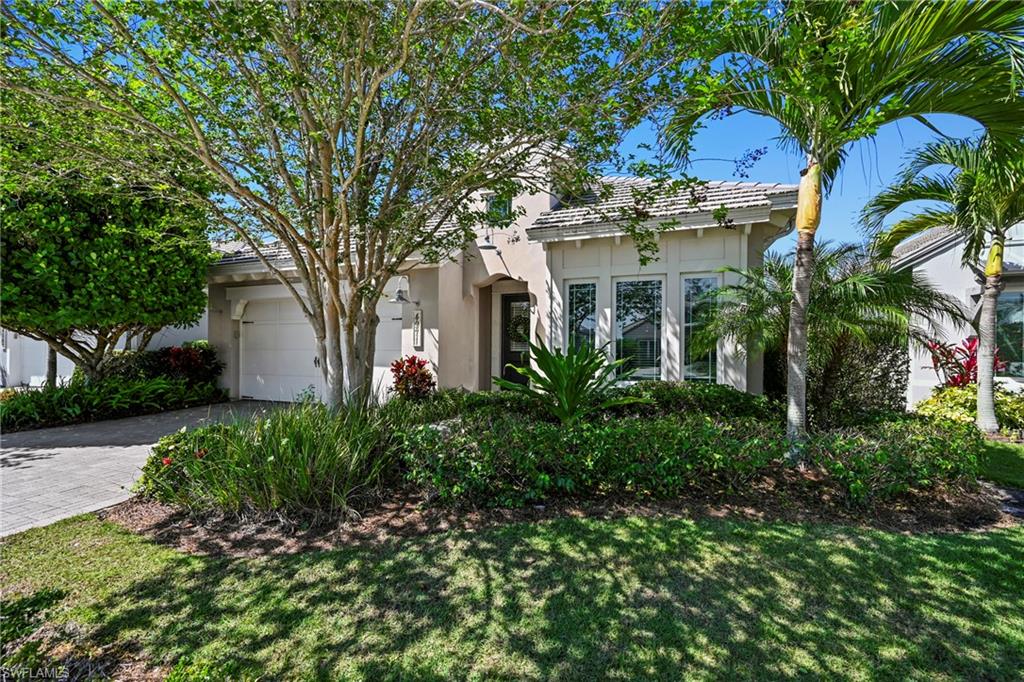 Exterior featuring a neutral stucco finish, white frame windows, a covered entry, an integrated garage, and professional landscaping