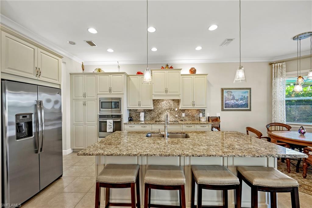 Expansive kitchen featuring a large island with an undermount sink and pendant lighting, light-toned cabinetry, stainless steel appliances, a built-in oven, and granite countertops with a matching backsplash