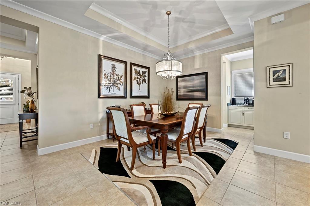 Recessed tray ceiling with crown molding, chandelier lighting, and neutral tile flooring