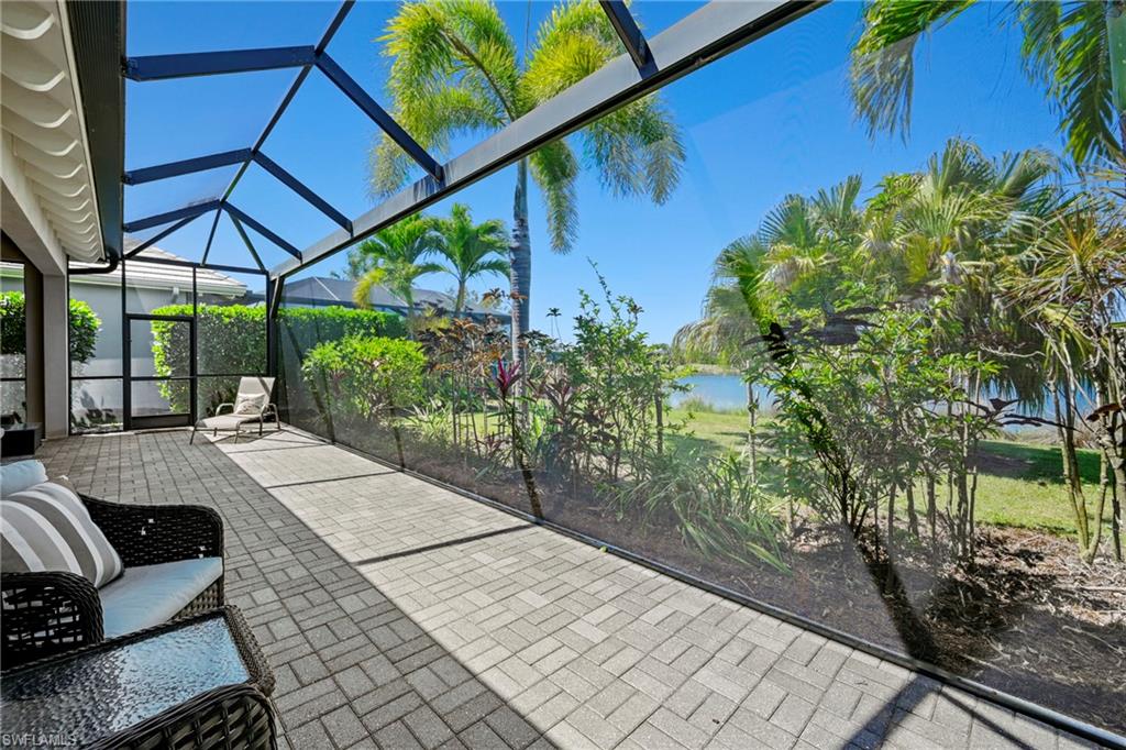Screened lanai featuring paver flooring, direct water frontage, and lush landscaping