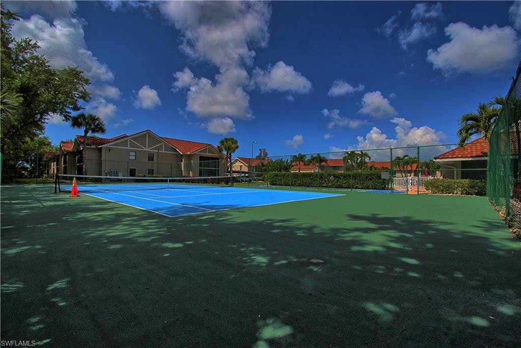 Outdoor tennis court featuring a blue playing surface and green surrounding area