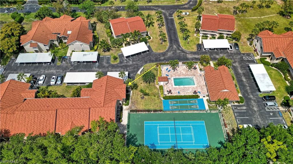 Community featuring multiple buildings with red tile roofs, swimming pool, tennis court, and covered parking areas