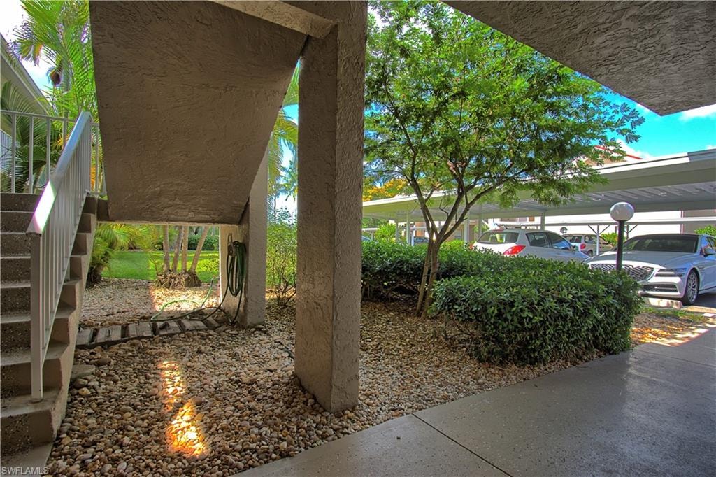 Covered parking structure featuring multiple vehicle spaces, mature landscaping, and an adjacent pedestrian pathway